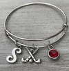 Personalized field hockey bangle bracelet with letter charm and red birthstone displayed on wooden background