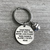 Inspirational softball keychain laid flat on wood surface, engraved charm in focus