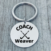Close-up of COACH Weaver engraved stainless steel keychain on gray wood surface