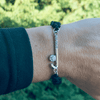 Close-up of wrist wearing the black rope bracelet with silver field hockey charm outdoors