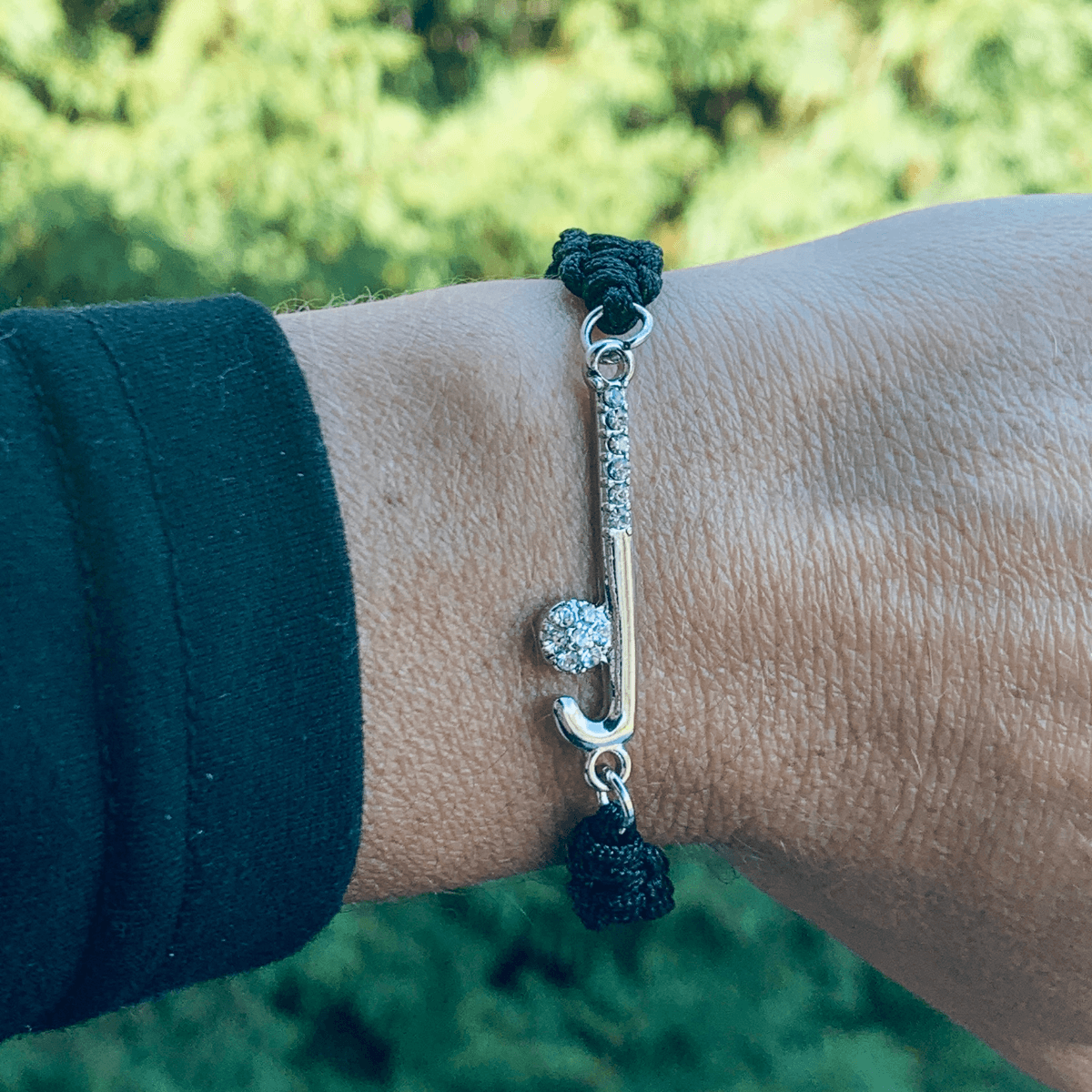 Close-up of wrist wearing the black rope bracelet with silver field hockey charm outdoors