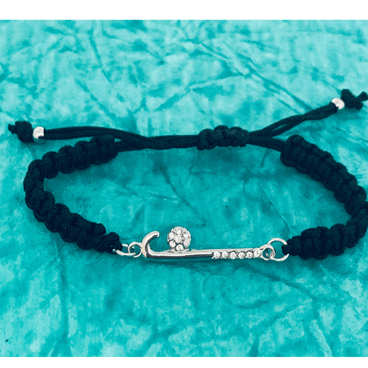 Field hockey bracelet with silver stick charm displayed on turquoise fabric background