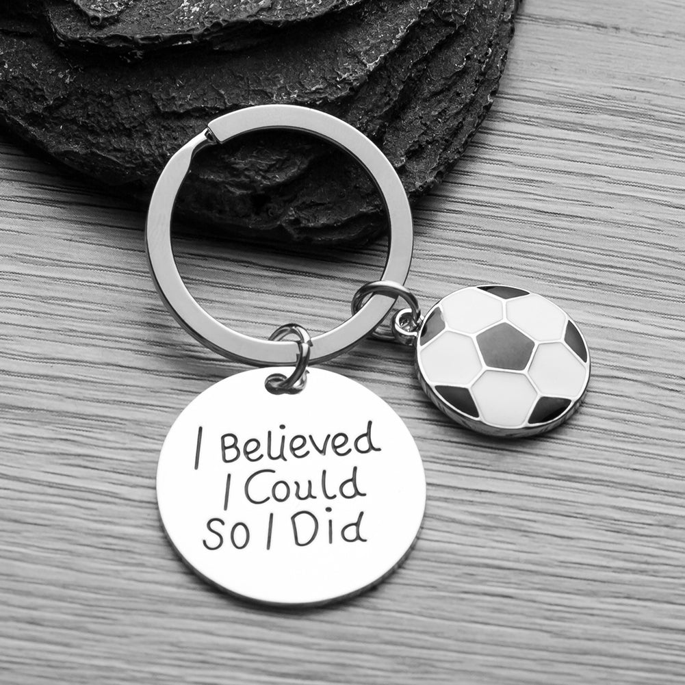 Soccer charm keychain displayed on black background with engraved inspiration quote