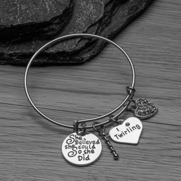 Twirling charm bracelet displayed on black background featuring heart charms and inspirational quote